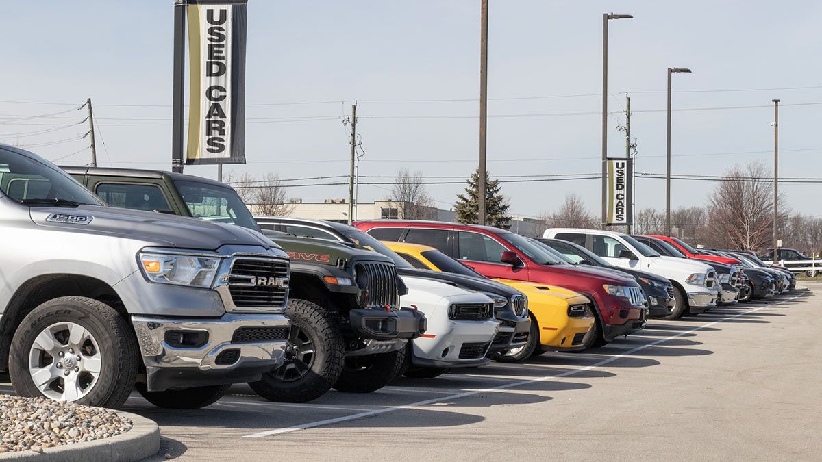 A line of used cars for sale at a dealership beneath a used cars sign