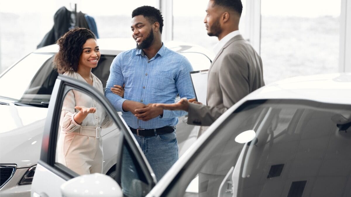 A couple talks with a car salesperson in front of a white sedan