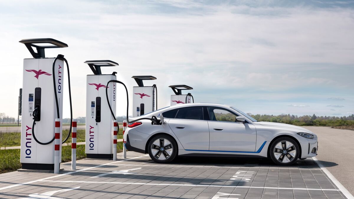 A 2023 BMW i4 electric sedan in white, seen in profile, plugged in to charge