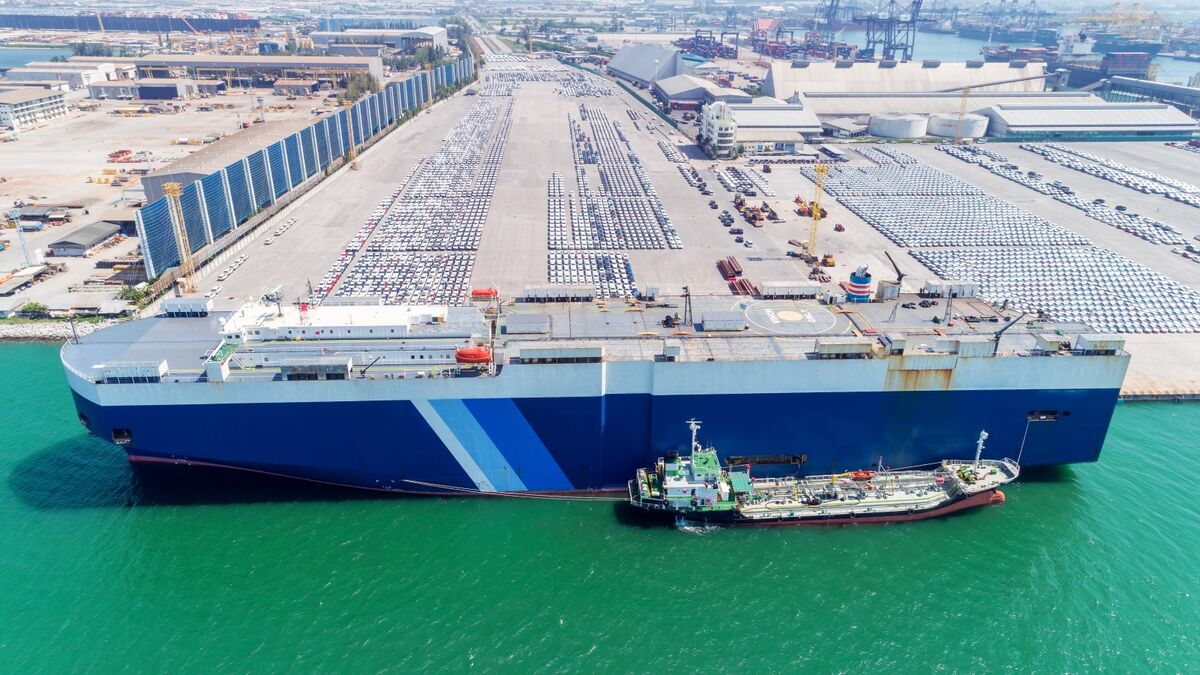 A car carrier ship in port next to thousands of recently-unloaded cars