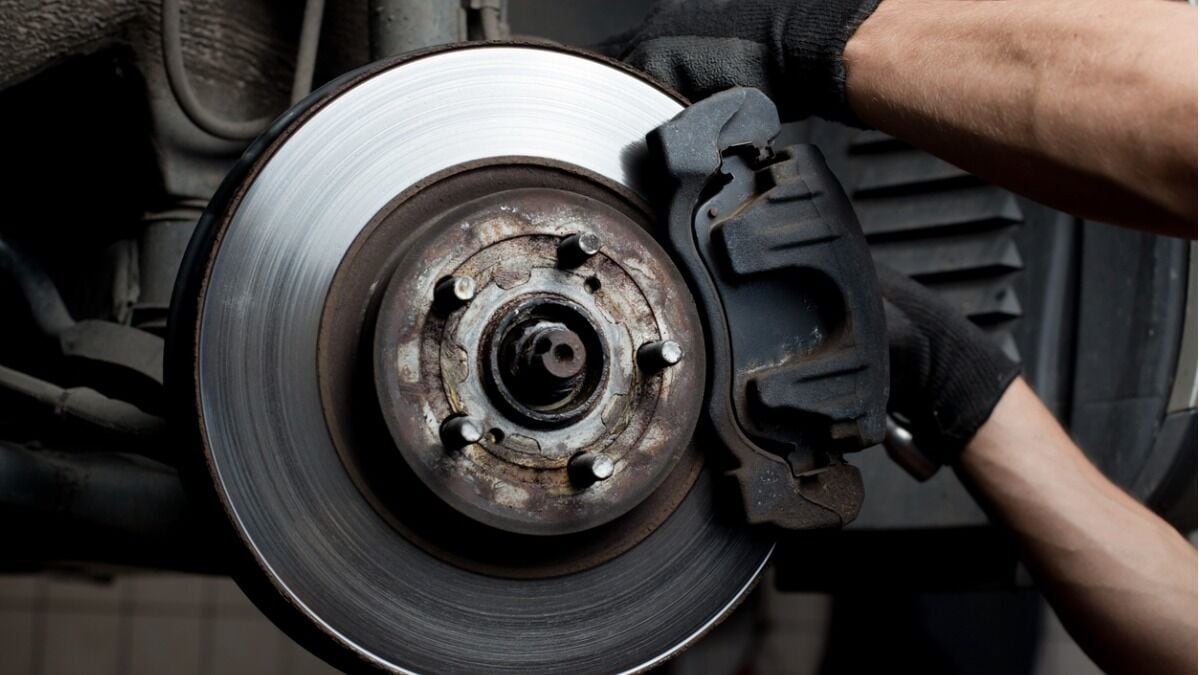 A mechanic wearing gloves works on a set of brake pads