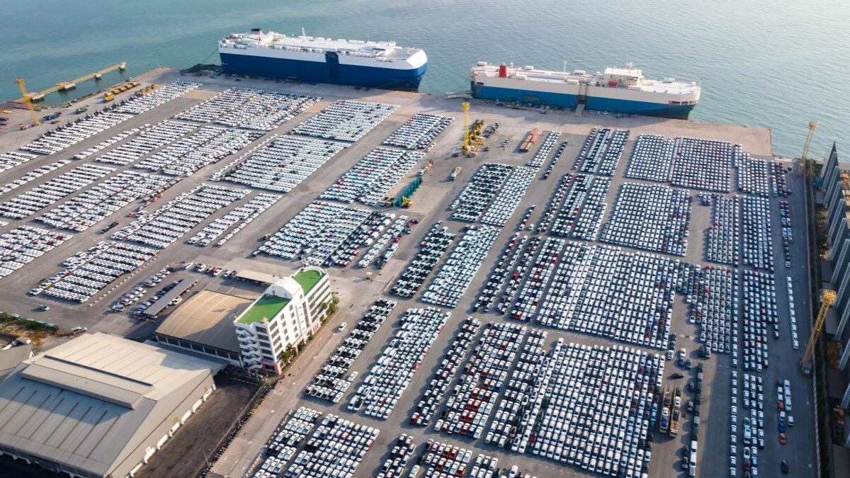 Thousands of cars lined up in port next to two roll-on/roll-off car carrier ships